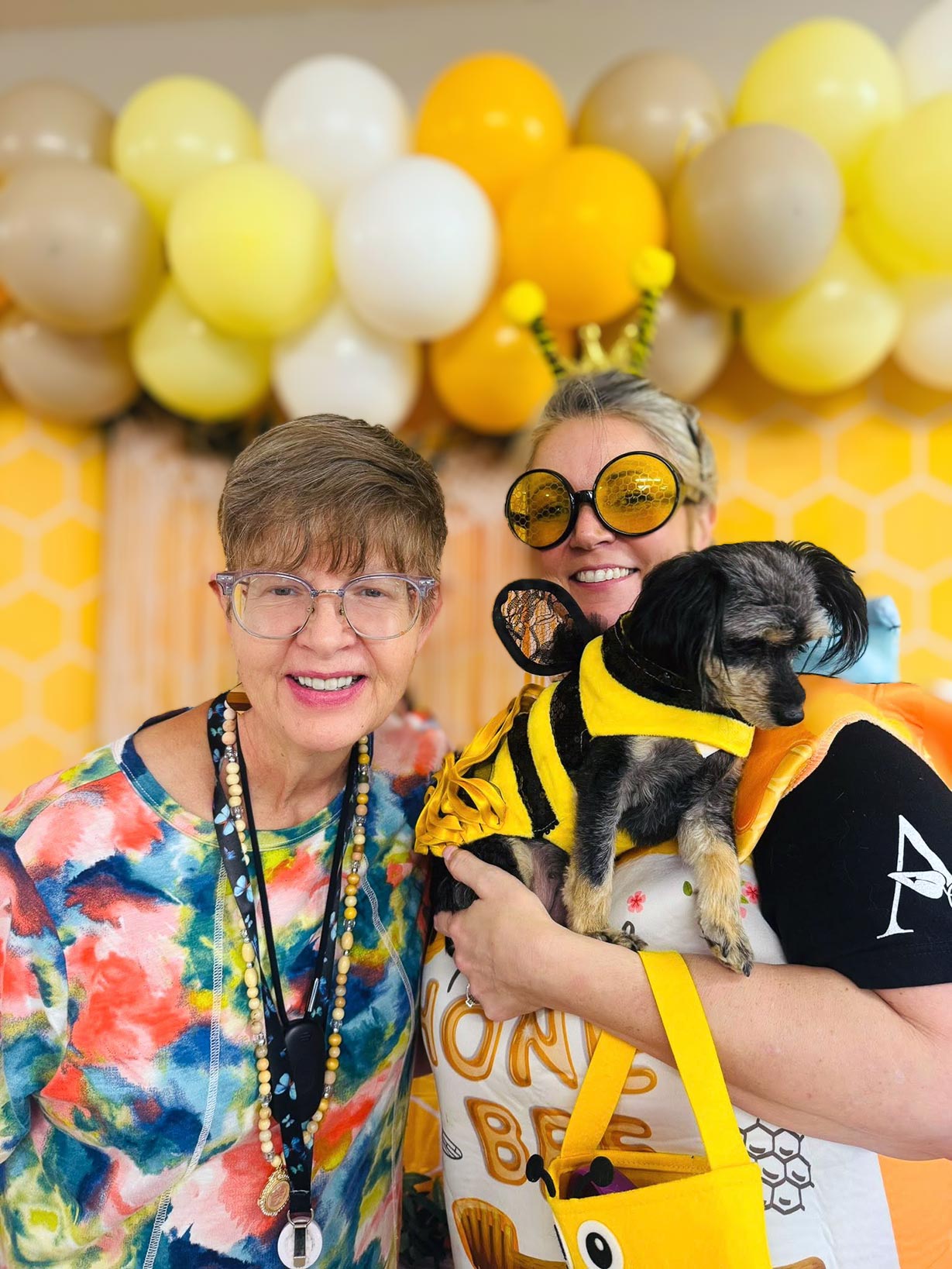 A woman poses with a team member wearing a bee-themed outfit and holding a dog dressed as a bee.