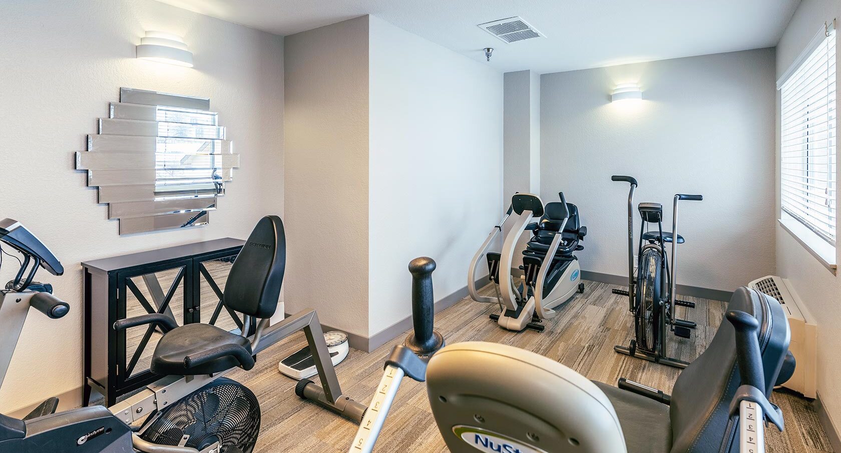 Senior living fitness room with seated exercise equipment, stationary bike, and bright natural light.