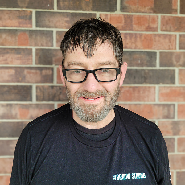 David Rick, Plant Operations Director at Buckingham Senior Living, smiling in a professional headshot, wearing glasses and a black shirt, with a brick wall background.