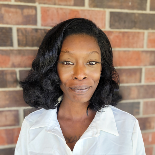 Larolyn Dodd, Business Office Director at Buckingham Senior Living, smiling in a professional headshot, wearing a white blouse, standing in front of a brick wall background.