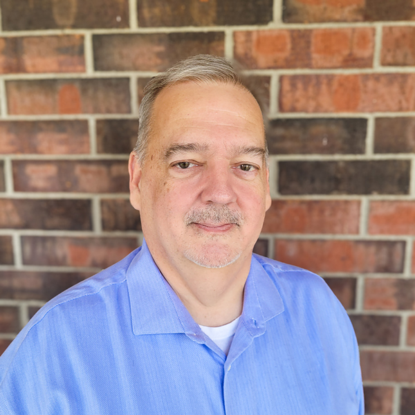 Marc Jacobs, Executive Director at Buckingham Senior Living, smiling in a professional headshot, wearing a light blue collared shirt, standing in front of a brick wall background.