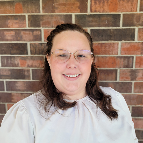 Marissa Moore, Resident Services Director at Buckingham Senior Living, smiling in a professional headshot, wearing glasses and a light blouse, standing in front of a brick wall background.